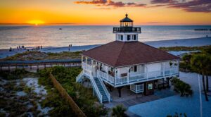 Boca Grande Lighthouse at sunset on Gasparilla Island with Gulf of Amemrica beach and orange sky in Southwest Florida