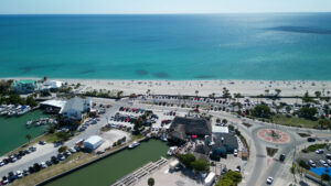 Aerial view of Englewood Beach Florida showing turquoise Gulf waters, beachfront parking, roundabout intersection, marinas, and coastal businesses along Manasota Key