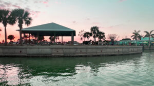 Sunset waterfront view of SandBar Tiki and Grille in Englewood Florida during an evening boat tour with calm Gulf Coast water and tropical palm trees