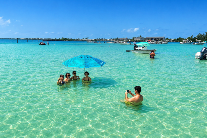 Relaxing at Boca Grande Sandbar | Southwest Florida Family and friends relaxing in the crystal-clear waters of Boca Grande Sandbar in Southwest Florida under a beach umbrella.