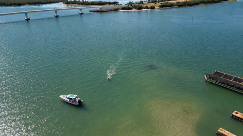 Drone view of Captain Pavel riding an e-foil back toward his anchored Axopar boat near the Historic Placida Trestle in Gasparilla Sound, Placida, Florida.