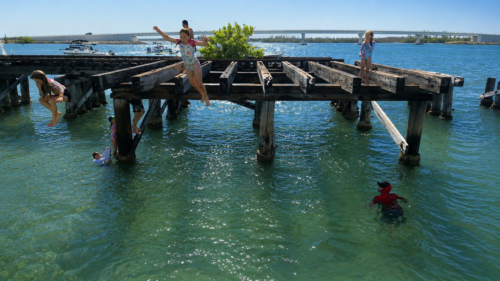 Children jumping from the historic Placida Trestle into the clear waters near Boca Grande Sandbar in Southwest Florida.Title
