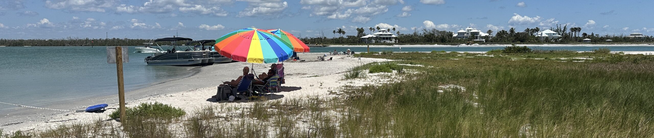 Visitors relaxing under a colorful beach umbrella at Ski Alley sandbar near Stump Pass in Englewood, Southwest Florida.