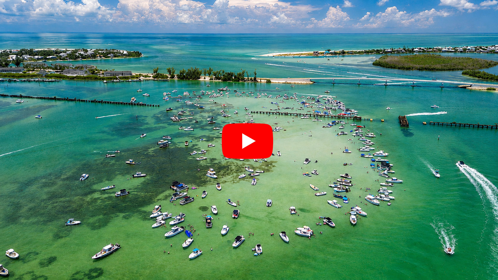 Aerial drone view of Boca Grande Sandbar in Gasparilla Sound, Florida, with dozens of boats anchored in crystal-clear turquoise water near Placida and Boca Grande Pass.