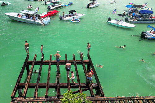 Drone view of people preparing to jump from the historic Boca Grande railroad trestle into the turquoise waters of Boca Grande Sandbar during the Independence Day celebration.