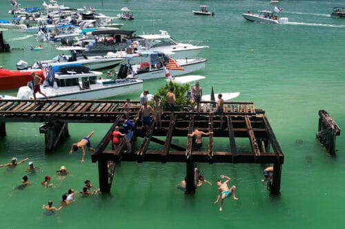 People jumping into the clear waters from the historic Boca Grande railroad trestle while boats gather nearby during the Independence Day celebration at Boca Grande Sandbar, Florida.