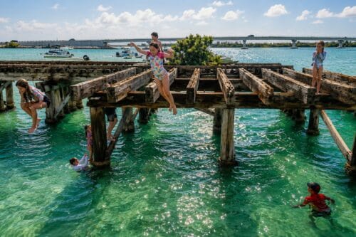 Children jumping into the clear waters of Gasparilla Sound from the remains of the historic Placida Trestle in Southwest Florida.