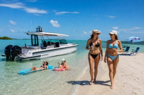 Luxury Axopar boat anchored at a Southwest Florida sandbar with guests walking along the beach and relaxing on floating loungers in shallow turquoise water.