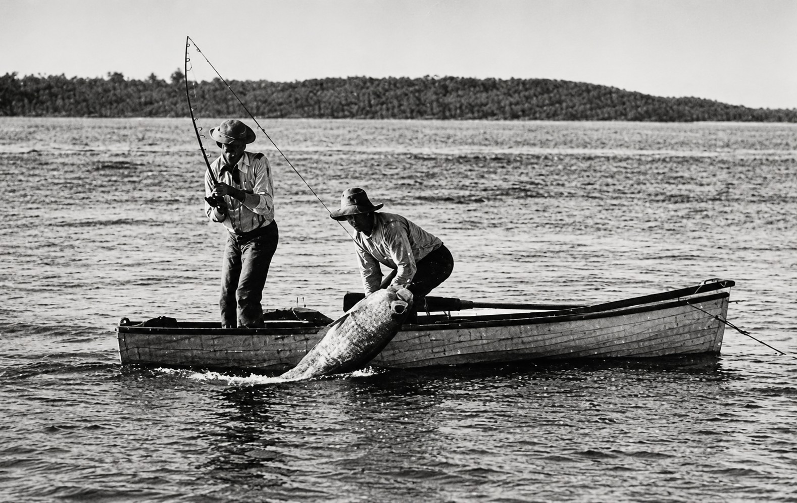 Historic photograph of two anglers landing a giant tarpon from a small boat in Gasparilla Pass near Boca Grande, Florida.