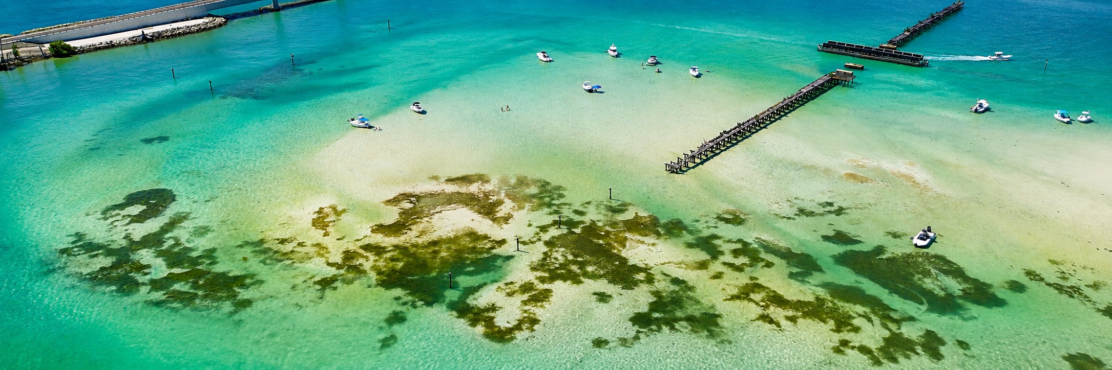 Aerial drone view of Boca Grande Sandbar on a weekday showing turquoise water, shallow sand flats, anchored boats, and historic railroad pier remains in Southwest Florida.
